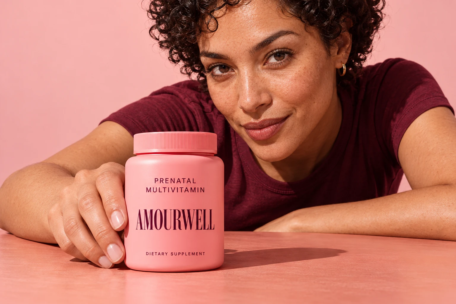 Woman leaning across a peach table with the pink Amourwell prenatal bottle