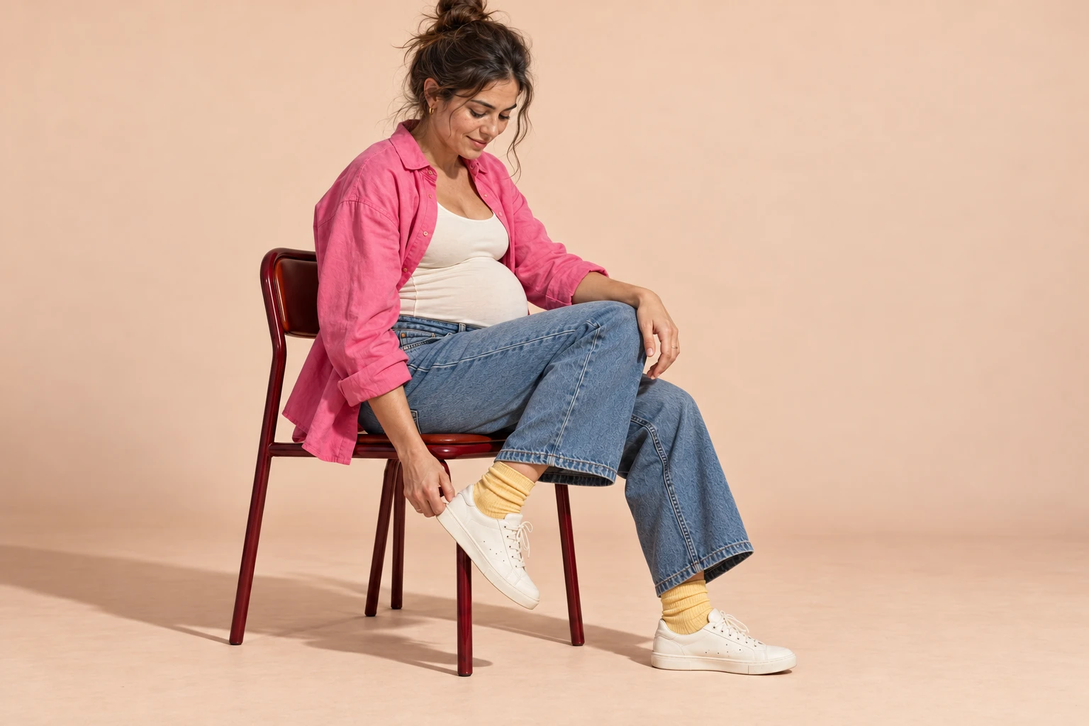 Pregnant woman in a pink shirt pulling on a sneaker while seated
